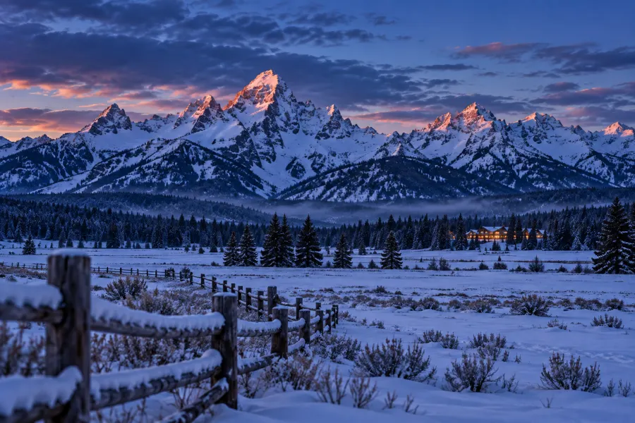 Snow-covered peaks catching the last alpenglow above a frozen meadow and dark spruce forest.